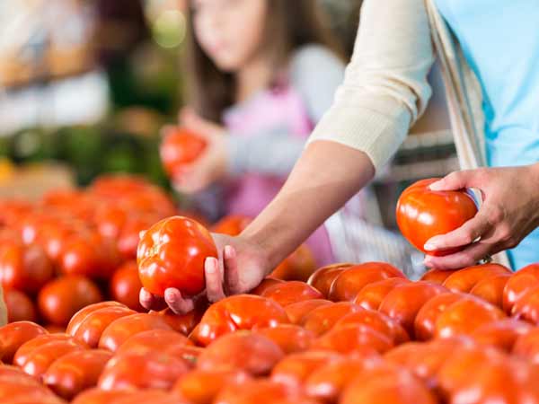 Image of a woman selecting tomatoes at a grocery store.
